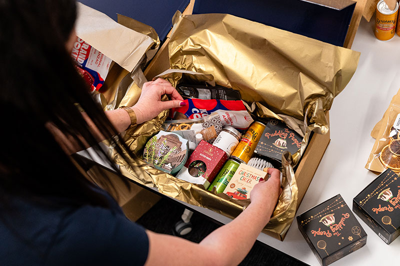 Volunteer packing a Christmas hamper filled with a variety of goods. 