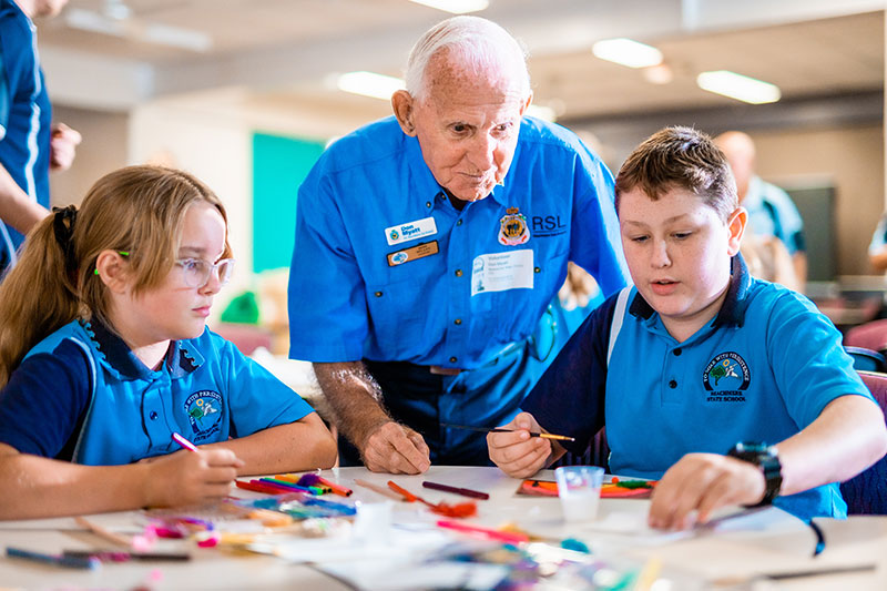 Don Myatt from RSL Beachmere Sub Branch helps students from the local school create postcards for veterans.